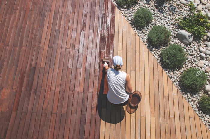 Persona barnizando un suelo exterior de madera natural.